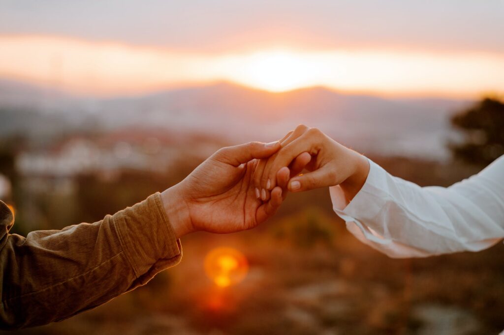 unrecognizable couple holding hands at sunset